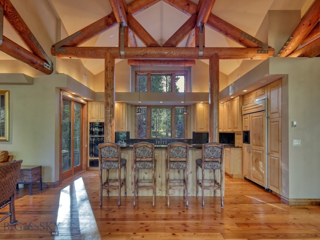 kitchen with beam ceiling, a breakfast bar, high vaulted ceiling, light hardwood / wood-style flooring, and paneled built in fridge