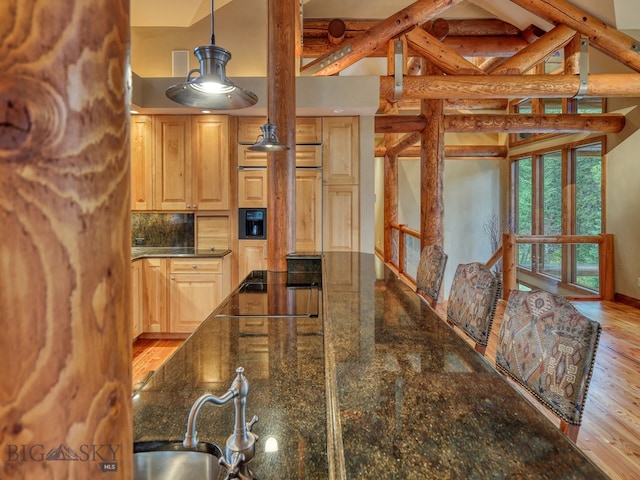 kitchen with backsplash, light brown cabinetry, dark stone counters, light hardwood / wood-style floors, and decorative light fixtures