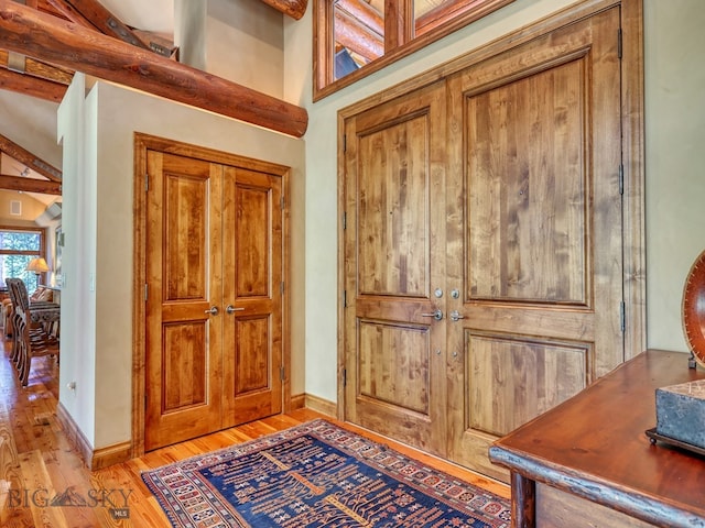 foyer entrance featuring a towering ceiling, light hardwood / wood-style flooring, and beam ceiling