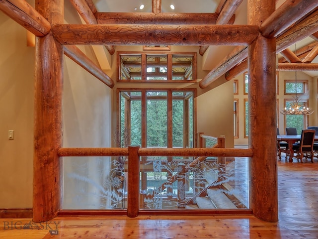 interior space with beam ceiling, a towering ceiling, wood-type flooring, and an inviting chandelier