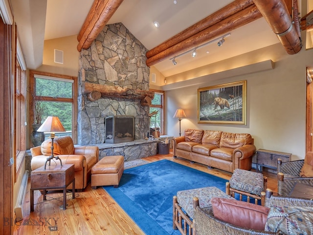 living room featuring a stone fireplace, vaulted ceiling with beams, rail lighting, a baseboard radiator, and light hardwood / wood-style floors