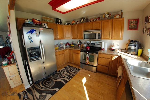 kitchen with appliances with stainless steel finishes, sink, and light hardwood / wood-style flooring