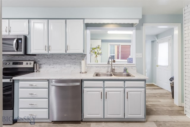 kitchen with decorative backsplash, light hardwood / wood-style floors, white cabinets, stainless steel appliances, and sink