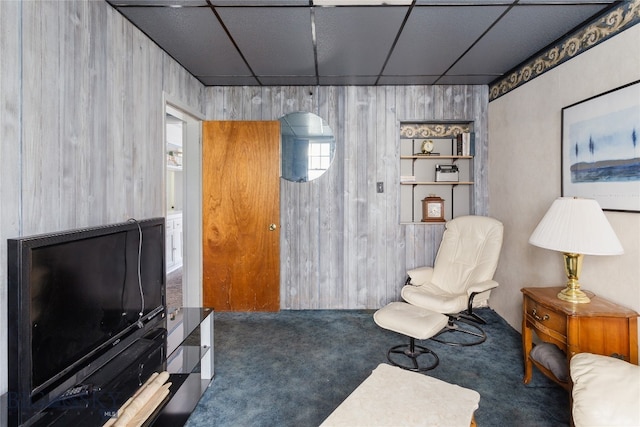 sitting room with a paneled ceiling, wood walls, and dark carpet