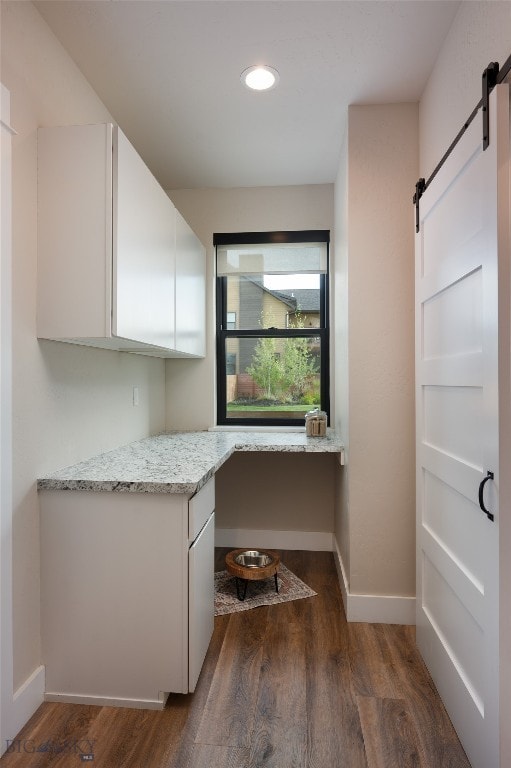 interior space featuring dark hardwood / wood-style flooring, white cabinets, light stone countertops, and a barn door