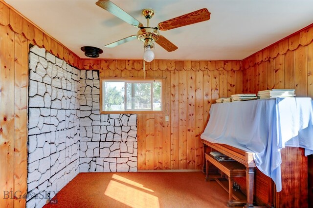 miscellaneous room with wooden walls, ceiling fan, and carpet flooring