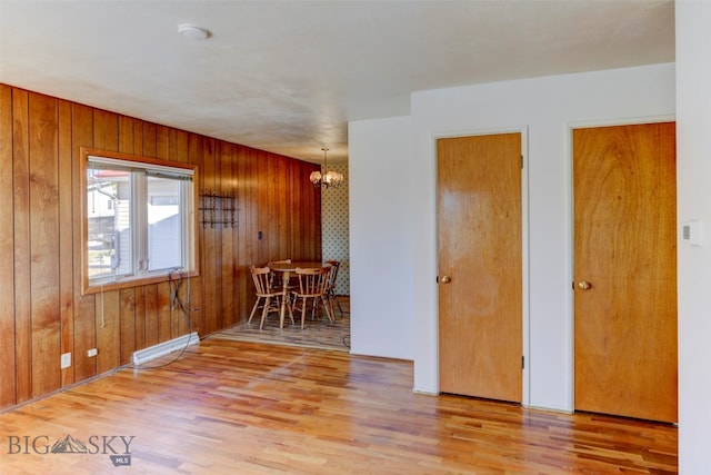 unfurnished room featuring a baseboard radiator, a chandelier, light hardwood / wood-style floors, and wood walls