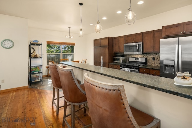 kitchen with pendant lighting, backsplash, dark wood-type flooring, stainless steel appliances, and a kitchen breakfast bar