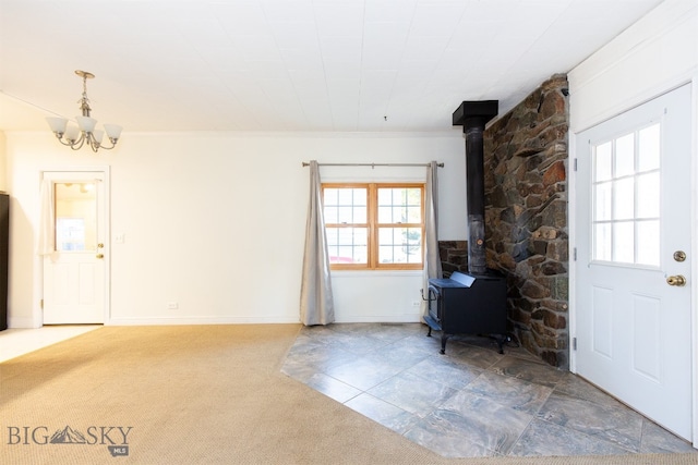 unfurnished living room with carpet floors, crown molding, a wood stove, and a notable chandelier