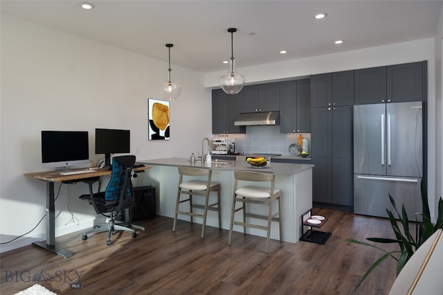 kitchen featuring decorative backsplash, a breakfast bar, stainless steel refrigerator, kitchen peninsula, and dark hardwood / wood-style floors