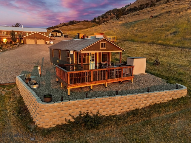 back house at dusk with a wooden deck, a lawn, a garage, and an outbuilding