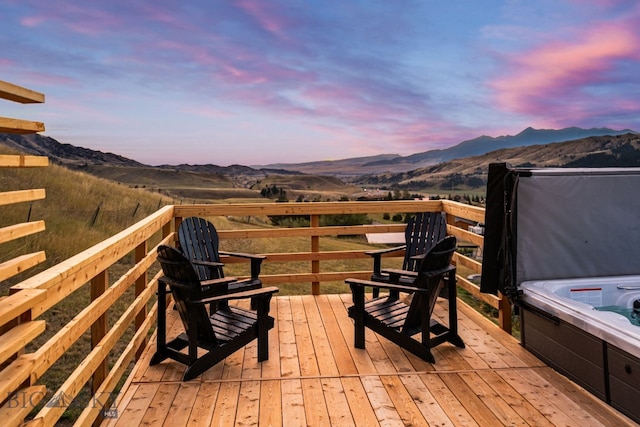 deck at dusk with a hot tub and a mountain view