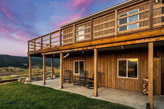 back house at dusk featuring a lawn, a patio, and a deck