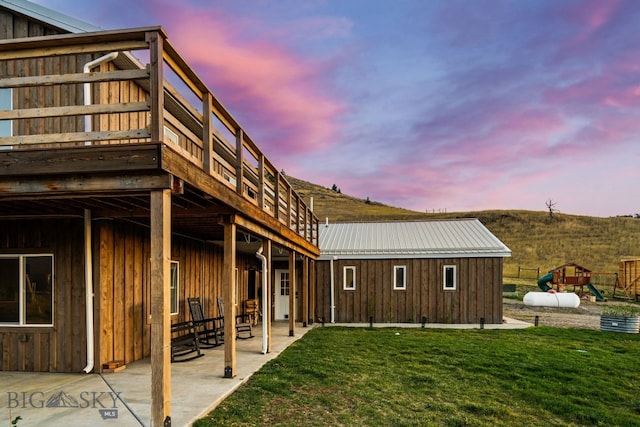 back house at dusk with a lawn, a patio, a playground, and a deck