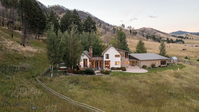 back house at dusk with a yard, a mountain view, and a patio area