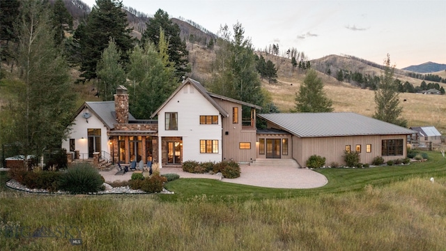 back house at dusk featuring a yard, a mountain view, and a patio area