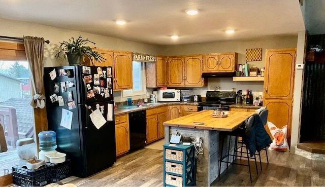 kitchen with a kitchen island, black appliances, a breakfast bar area, light hardwood / wood-style floors, and butcher block counters