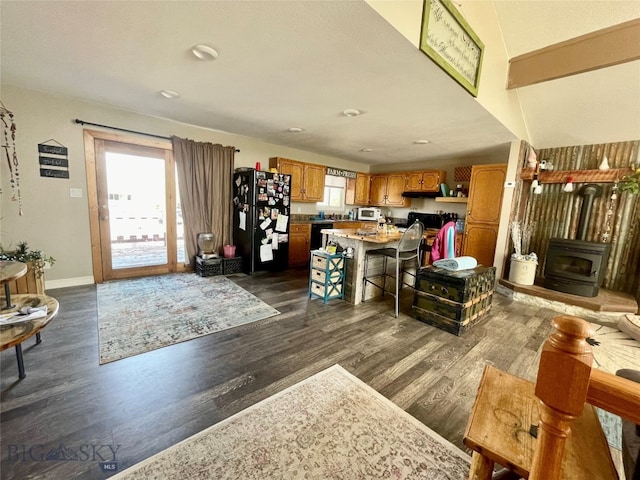 living room featuring a wood stove, vaulted ceiling, a healthy amount of sunlight, and dark hardwood / wood-style flooring