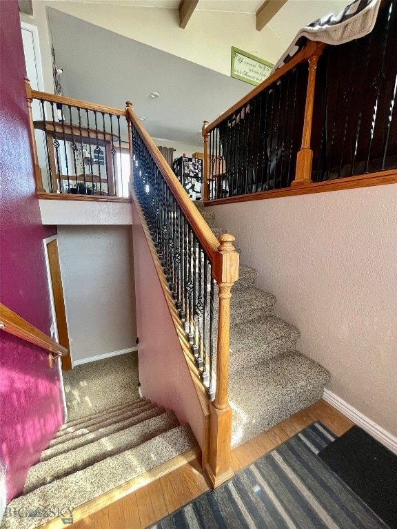 staircase featuring lofted ceiling with beams and hardwood / wood-style floors