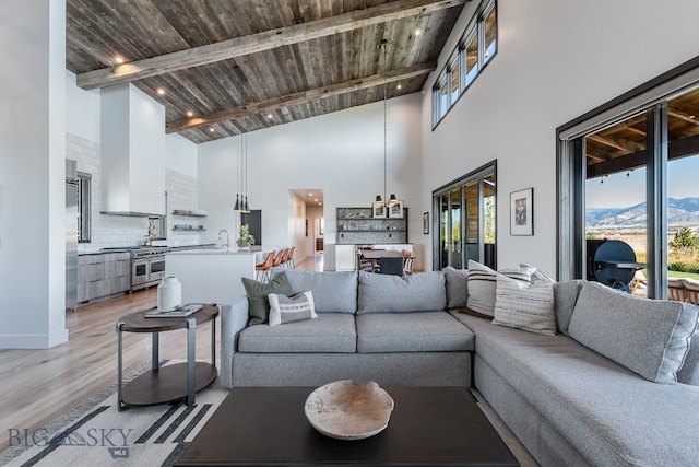 living room featuring beam ceiling, wooden ceiling, sink, light wood-type flooring, and high vaulted ceiling