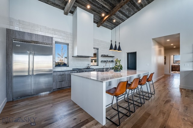 kitchen with dark wood-type flooring, a kitchen bar, appliances with stainless steel finishes, light stone counters, and high vaulted ceiling