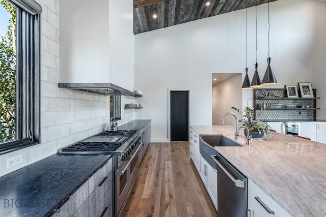 kitchen with appliances with stainless steel finishes, wall chimney exhaust hood, white cabinets, and pendant lighting