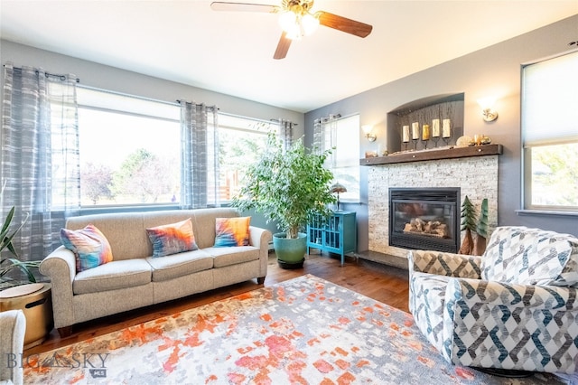 living room with wood-type flooring, a stone fireplace, and ceiling fan