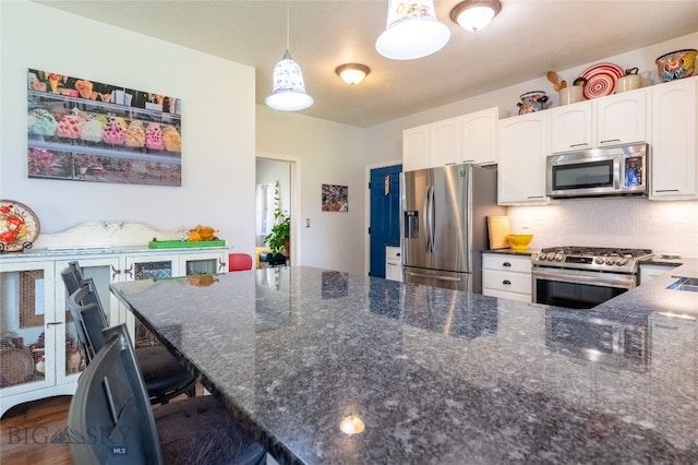 kitchen featuring appliances with stainless steel finishes, a kitchen breakfast bar, dark stone countertops, white cabinets, and pendant lighting