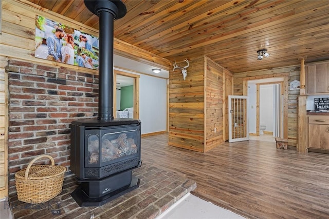 unfurnished living room featuring wood ceiling, a wood stove, wood walls, baseboards, and wood finished floors