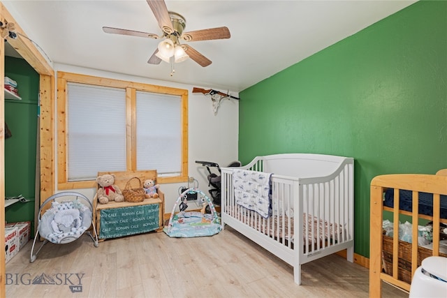 bedroom with ceiling fan, a nursery area, and hardwood / wood-style floors