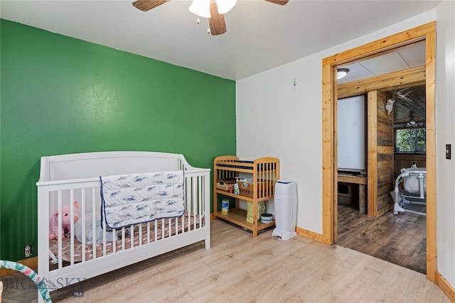 bedroom featuring light hardwood / wood-style flooring, ceiling fan, and a crib