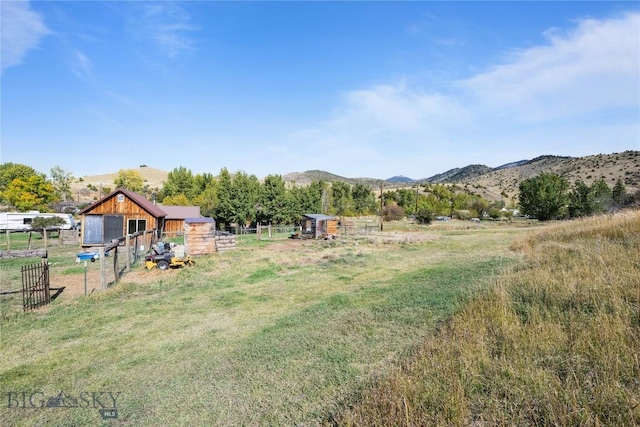 view of yard featuring a mountain view, fence, an outbuilding, and a rural view