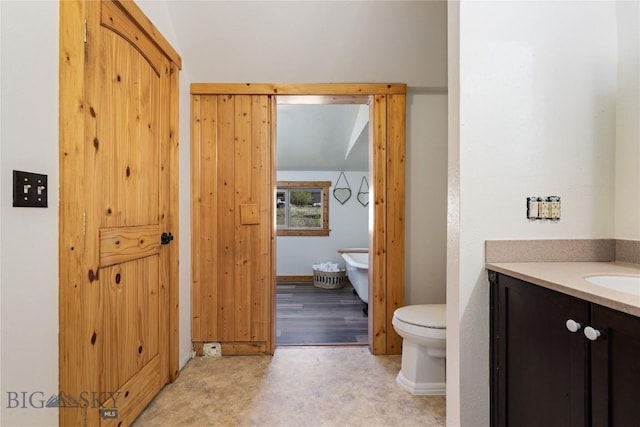 full bathroom with toilet, a soaking tub, and vanity
