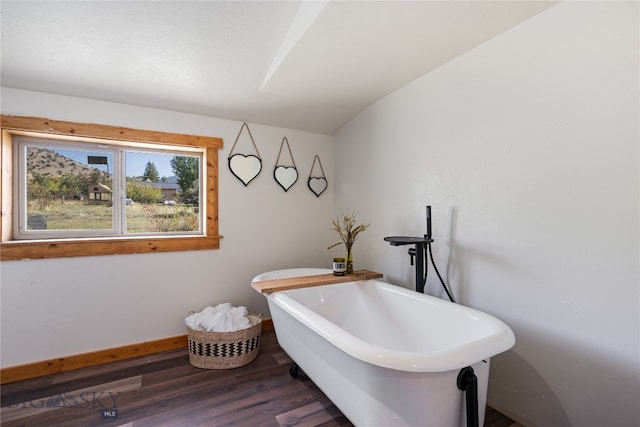 bathroom with lofted ceiling, a tub, and hardwood / wood-style floors