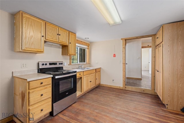 kitchen with a sink, light countertops, stainless steel range with electric stovetop, light brown cabinetry, and wood finished floors