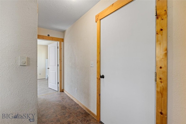 hallway featuring baseboards and a textured wall