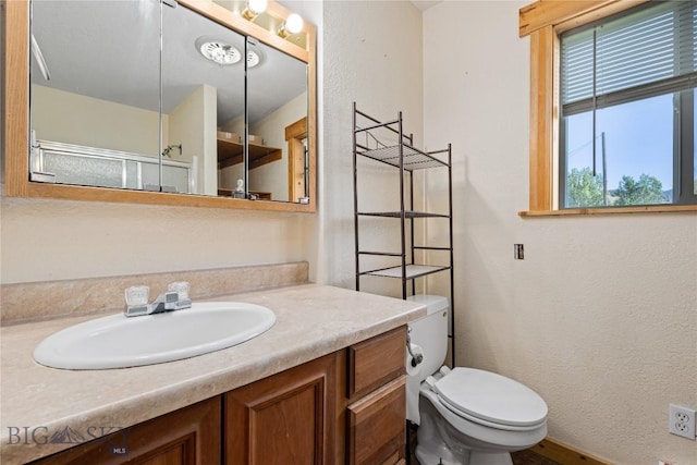 bathroom featuring toilet, a textured wall, and vanity