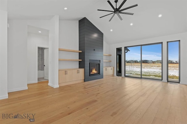 unfurnished living room featuring a large fireplace, light hardwood / wood-style floors, high vaulted ceiling, and ceiling fan