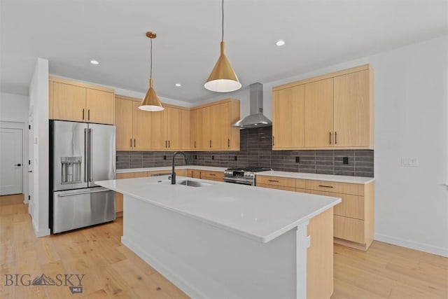 kitchen with appliances with stainless steel finishes, wall chimney exhaust hood, light brown cabinets, light hardwood / wood-style flooring, and an island with sink