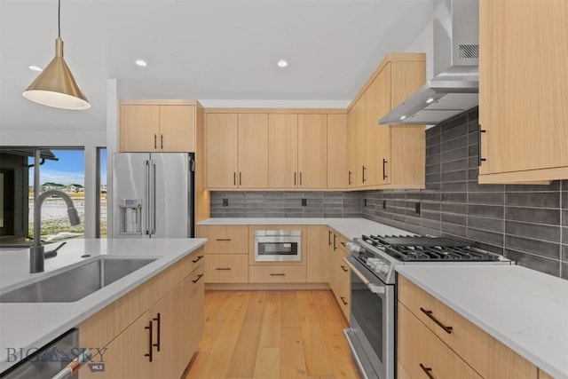 kitchen with sink, wall chimney exhaust hood, stainless steel appliances, light brown cabinetry, and light wood-type flooring