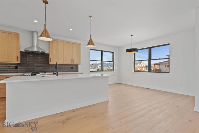 kitchen with light brown cabinets, light wood-type flooring, decorative light fixtures, and wall chimney range hood