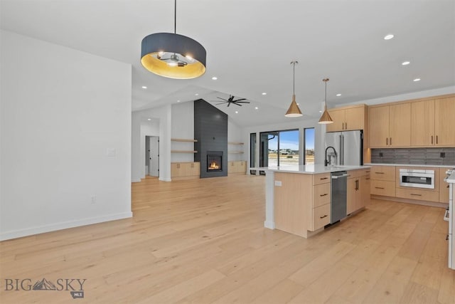 kitchen featuring decorative light fixtures, light brown cabinets, an island with sink, and vaulted ceiling