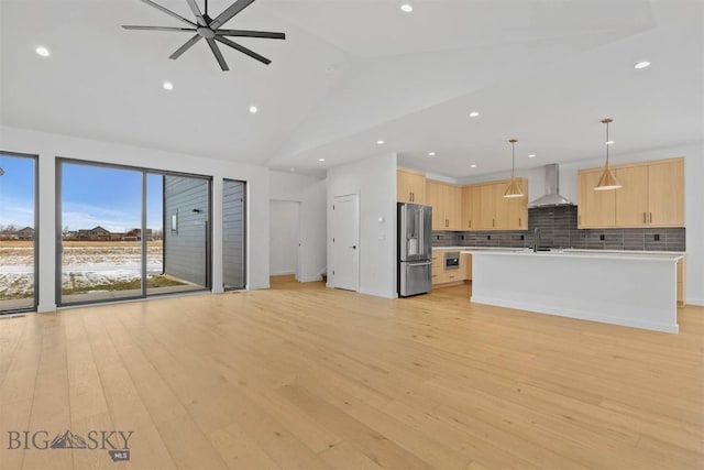 kitchen with wall chimney range hood, hanging light fixtures, stainless steel refrigerator with ice dispenser, light wood-type flooring, and light brown cabinetry