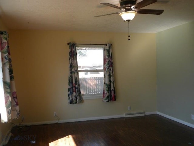 spare room featuring dark wood-type flooring, baseboard heating, and ceiling fan