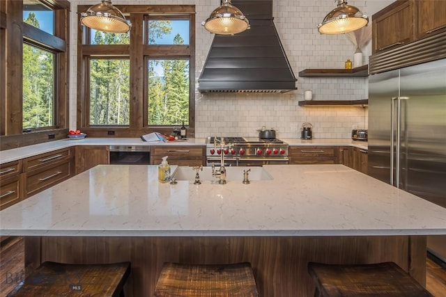 2250 Outlook Trl, Big Sky, MT 59716 - kitchen featuring premium appliances, range hood, a center island with sink, decorative backsplash, and light stone countertops