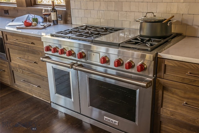 kitchen with dark wood-type flooring, range with two ovens, and tasteful backsplash