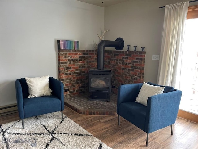 sitting room with baseboard heating, a wood stove, a wealth of natural light, and wood-type flooring