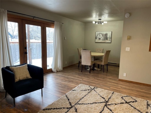 dining space with wood-type flooring, a baseboard heating unit, and a notable chandelier