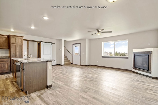 kitchen featuring light stone counters, ceiling fan, an island with sink, light hardwood / wood-style flooring, and a barn door