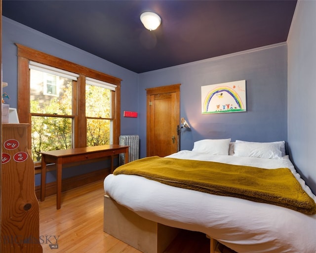 bedroom featuring light wood-type flooring, crown molding, and radiator